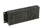 This rectangular slab of dark, textured material looks like a Vestil Laminated Dock Bumper 12 X 36 X 6 In, complete with two metal mounting brackets on each end. Its surface is uneven and weathered, featuring visible horizontal grains and lines.