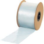 A large roll of transparent plastic film, similar to the MH-USA 2 x 4 - 1.54 Mil Poly Bags on a Roll (4000/Roll), partially unspools, shimmering in the light, while being wound around two brown cardboard discs serving as spool ends.