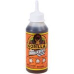 The 8 oz. Gorilla Glue® bottle with an orange label features the iconic Gorilla logo. It highlights its versatility on wood, stone, metal, ceramic, foam, and glass and comes with a white nozzle cap for precise application.