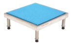 A small metal platform with four legs and a blue square cushioned top, similar to the Vestil Adj Alum Stand 9.5-15.5 H 24 X 24. The legs feature black rubber caps, edges are reinforced, and its functional design includes a label on the side, adjustable between 9.5-15.5 inches in height.