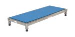 A rectangular platform with a blue cushioned top and sturdy metal frame, similar to the Vestil Adjust Ss Stand 6.75-8.75 H 19 X 48, features four black rubber-tipped legs and a side label, resembling a grooming table or low bench.