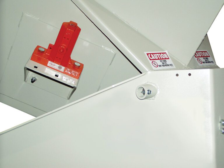 Close-up of a Vestil Corner Tilt Optional Power Vibration with a red lever and optional power functionality. The mainly white structure, adorned with caution labels and safety symbols, ensures efficient operation in demanding environments.
