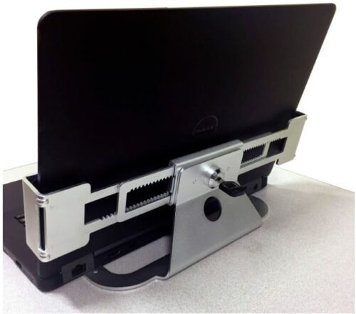 A laptop docked in a metallic horizontal docking station, featuring adjustable sliding grips and a central locking mechanism, placed on a light-colored surface.