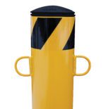 Yellow bollard with black diagonal stripes near the top, featuring two looped handles for D-ring chain attachment, similar to a Vestil Bollard D-Ring Chain Attachment.