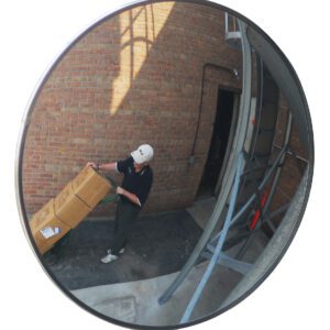 A Vestil Convex Mirror Outdoor 30 Ft Distance reflects a person with a cap pushing a hand truck loaded with boxes by a brick wall near an open door, enhancing safety and efficiency in busy outdoor areas.