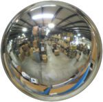 A fisheye view of a warehouse enhanced by a Vestil Convex Mirror Outdoor 35-40 Ft 7 In Deep captures rows of shelves brimming with boxes, revealing the ceiling, floor, and storage areas in one wide-angle sweep.