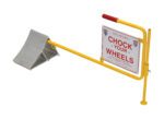 The Vestil Aluminum Wheel Chock With Flag is a sturdy metal design featuring a ridged surface and an attached Chock Your Wheels sign mounted on a yellow frame.