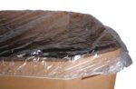 A large cardboard box is covered with a Vestil Elastic Gaylord Cover 64 In. The clear cover stretches securely over the 64-in top, with some overhang on the sides, while the corrugated texture of the box remains visible along its edges.