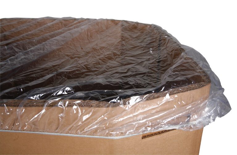 A large cardboard box is covered with a Vestil Elastic Gaylord Cover 64 In. The clear cover stretches securely over the 64-in top, with some overhang on the sides, while the corrugated texture of the box remains visible along its edges.