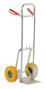 The Vestil Fold-Down Aluminum Hand Truck-Yel Ureth stands upright, highlighting its metallic sheen and red handles, complemented by yellow urethane wheels on a tall frame and flat base for easy item transport.