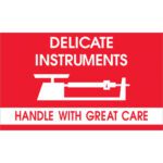A red and white sign, like the MH-USA 3 x 5 labels (500/Roll), shows a balance scale graphic. It reads DELICATE INSTRUMENTS above and HANDLE WITH GREAT CARE below.