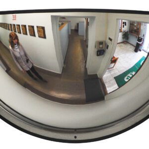 A woman is reflected in a Vestil Dome Mirror 180 Degree 32 Ft Distance while walking down a hallway with framed pictures. An open area with chairs and a rug is visible in the reflection.