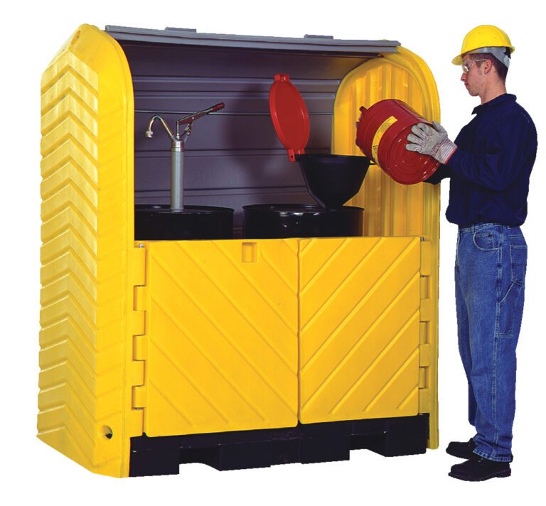 A worker, wearing safety gear, pours liquid from a red container into a funnel on a black drum inside a Vestil Hard Top Drum Storage-2 Drum With Drain while the yellow chemical storage cabinet stands open, displaying its organized contents.