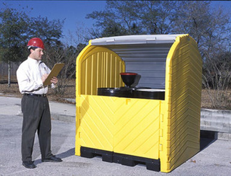 A man in a red hard hat inspects a Vestil Hard Top Drum Storage-4 Drum With Drain, featuring a curved, ribbed roof and barrels with funnels, against a backdrop of trees and clear sky.
