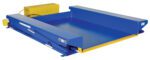 The blue industrial dock leveler with yellow edges, safety labels, and a power unit pairs with the Vestil Ground Lift Scissor Table 4K 52 X 73 to bridge gaps between docks and trucks, ensuring a stable loading and unloading platform.