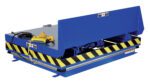 The Vestil Lift & Side Link Tilt Scissor Table 2K showcases a blue hydraulic lift table with yellow and black safety stripes, featuring a cable-connected handheld control unit on top. It has a sturdy industrial design when lowered.