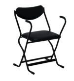 The Vestil Folding Arm Chair features a black metal frame, cushioned seat and backrest, with elegantly curved armrests. Its minimalist design adds versatile style, contrasting beautifully against the white background.
