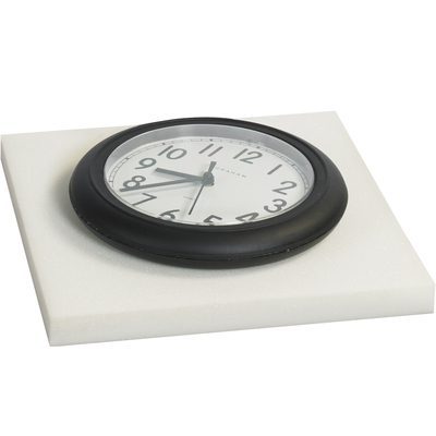 FSW121205.jpg A round black wall clock with a white face and black numerals is placed on an MH-USA 1/2 x 12 x 12 White Cloud Foam Sheet from a batch of 96 sheets per case, showing the time as around 10:09.