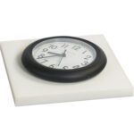 A round black wall clock with a white face and black numbers, showing 8:20, sits on an MH-USA 1 x 12 x 12 White Cloud Foam Sheet from a case of 48 sheets. The clock hands are black, with the second hand in red.