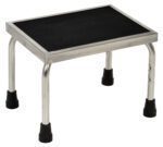 The Vestil Stainless Steel Foot Stool is a compact, rectangular step stool with a black non-slip surface. It features four silver metal legs, each capped in black plastic to ensure stability.