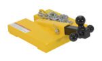The Vestil Fork Lift Hitch Attachment is a yellow trailer hitch adapter featuring a black cube with three diverse-sized towing balls, and is secured by a silver chain wrapped around its base, alongside a caution label on the yellow metal.