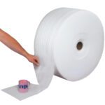 A person unrolls a MH-USA 1/16 x 12 x 900 Parcel Ready Perforated Air Foam Roll (900/Roll) and wraps it around a pink mug against a white background.