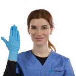 A person with brown hair is wearing blue medical scrubs and a blue glove on their right hand, raised in a wave. They are smiling and standing against a plain white background. The scrubs have the text Grip Protect on them.