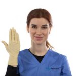 A person with brown hair in a blue medical uniform holds up their hand wearing a beige glove. The uniform has a logo on it. The background is white.