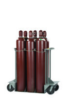 Six large brown gas cylinders are securely upright on a Little Giant Gas Cylinder Truck. This wheeled metal cart with a secure chain and handles allows easy maneuvering, and each cylinder features labels and protective caps for safety.