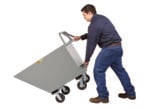 A person in a blue shirt and jeans tips the Little Giant Hopper Truck with Ergonomic Handle. The gray industrial cart, with four wheels, is tilted forward, indicating use for transporting or dumping materials against a white background.