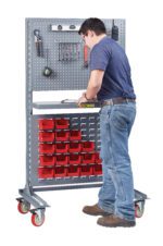 Dressed in a blue shirt and jeans, a person stands at the Little Giant Heavy-Duty Mobile Work Center - Single Sided (Frame Only), utilizing its red storage bins and pegboard full of tools to skillfully work on the surface.