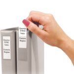 A hand retrieves a gray binder labeled Quarter Two Sales, Eastern Region nestled between two binders, each with perfectly sized white labels for the MH-USA 2 3/4 x 3 5/8 Binder Top Loading Self-Adhesive Holder (60/Case). Quarter One Sales, Eastern Region is positioned next to it.