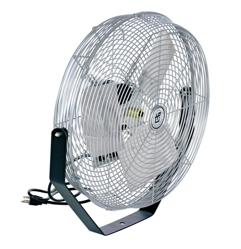 A large metal floor fan with a wire cage and three blades, resembling the Vestil Loading Light Fan Option, sits on a sturdy black stand. It has a neatly coiled power cord at the base.