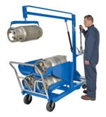 A person in safety gear operates the blue Vestil LP Tank Truck, which holds multiple kegs with its 6-tank capacity. The hydraulic arm elevates one keg while sturdy wheels ensure easy mobility.