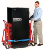 A man in a light blue shirt and beige pants uses a red Vestil Vend. Machine-Furn. Movers 6000 Lb Cap hand truck to move a large black safe, secured with blue straps, against a plain white background.