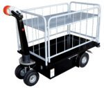 The Vestil Traction Drive Cart-1 Shelfs-Side Load features a sleek black base with four wheels and a steering handle. It includes side rails to secure cargo and an upper metal shelf for extra storage, ideal for efficient, side-load transport.