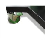 A metal caster wheel with a green brake is attached to the black frame of a piece of furniture, possibly a table or cart, on a white background.