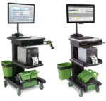 Two mobile workstations with monitors, keyboards, printers, and green baskets on wheels. They also feature attached barcode scanners and green battery packs at the base, designed for use in warehouse or industrial settings.