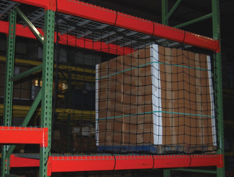 In a dimly lit warehouse, cardboard boxes on red and green industrial shelving are secured with Vestil Nylon Pallet Rack Netting 111 X 96 In.