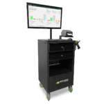 A black mobile workstation cart with the Newcastle Systems logo, featuring a mounted monitor displaying charts and graphs, a label printer, and drawers. The cart is on green wheels, designed for industrial or office use.