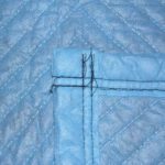 Close-up of a blue quilted fabric with black stitching in a cross pattern, similar to the durable texture of Vestil General Duty Moving Pads Cotton 12 Pack. The fabric looks textured, with evenly spaced parallel lines forming a geometric design.