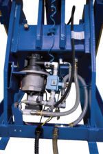 A close-up of a mechanical apparatus with interconnected metal components, featuring the Vestil LLH Rotary Air/Oil Handheld Push-Button, hoses, and a motor in a blue frame. Various pipes and cables are visible, indicating complex engineering with rotary functionality and handheld controls.