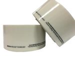 Two rolls of Vestil Industrial Racking Labels 1 In 100 Pc are displayed, one laying flat and the other leaning against it. Featuring HOLD & RELEASE TECHNOLOGY, these white labels with black text include the website labelplacard.com and patent details.