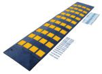 The Vestil Rubber Speed Hump 23.5 X 108 Concrete has a black surface with yellow reflective squares for visibility, a textured pattern for traction, and is secured to concrete with metal bolts and screws.