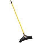 The Rubbermaid® Maximizer™ Push Broom - 18 with black bristles and a long handle stands upright against a white background, showcasing its vibrant yellow head, ready to tackle any mess.