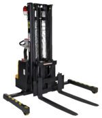 The image shows a Vestil Adjustable Extendable Fork Stacker in black, featuring long forks and a control handle. It has a yellow base with striped safety markings, designed for efficient lifting and transport of heavy loads.