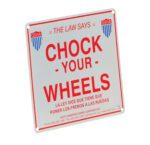The square safety sign displays The Law Says Chock Your Wheels in English and Spanish with OSHA logos, featuring the Vestil Aluminum Enamel Wheel Chock Sign 9.75 In, and includes Vestil Manufacturing Corporations contact details at the bottom.