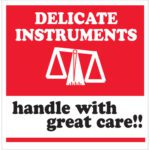 The MH-USA 4 x 4 label has a red background with DELICATE INSTRUMENTS in bold white and a scale icon on top. Below, handle with great care! is printed in black on white. This Delicate Instruments - HWC design comes in rolls of 500 labels.