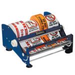 The MH-USA 12 Table Top Label Dispenser, featuring a sleek metal and plastic stand, comes with three label rolls for warnings on fragility, refrigeration instructions, and handling precautions, ensuring easy dispensing for all packaging needs.