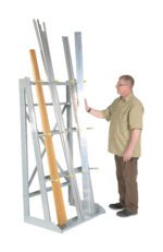 A man in a khaki shirt and brown pants carefully places long metal beams onto the Vestil Vertical Floor Mounted Rack W/ 2000 Lb, which also holds wooden beams, set against a plain white background.